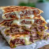 Steam rises from a crispy flour tortilla filled with Cheesy Griddled Smashburger Quesadillas, served with a creamy mayo-mustard sauce and pickles on the side.