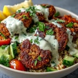 Crispy baked falafel sits on fluffy quinoa with fresh cucumber, tomatoes, and green onions, all drizzled with creamy garlic tahini sauce.