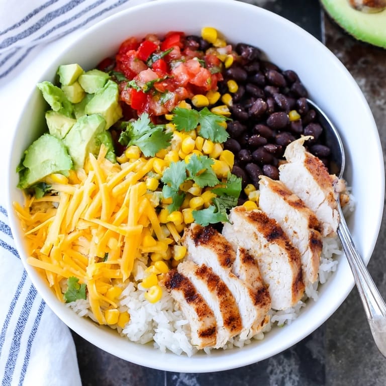 A close-up of a colorful Spicy Chicken Burrito Bowl topped with cilantro, lime wedges, and melted cheese.