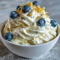 Delicate Lemon Fool dessert in a glass, topped with fresh lemon zest and a shortbread biscuit for a sweet crunch.