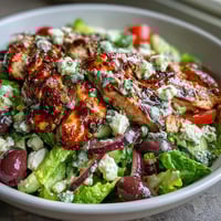 Greek Salad Bowl with Grilled Chicken, featuring tender, juicy chicken over crisp Romaine and fresh vegetables, drizzled with tangy lemon-oregano dressing.  